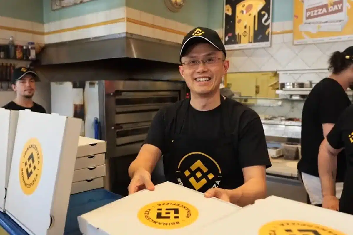 Changpeng Zhao (CZ) wearing a Binance apron and hat while serving pizza boxes, illustrating how modern exchanges celebrate bitcoin nostalgia during Pizza Day events.